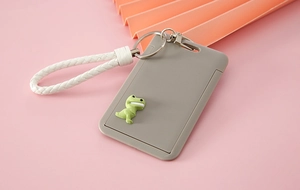 Close-up of gray slide card holder with white braided lanyard and green dinosaur charm