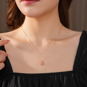 Close-up of gold plated necklace with a round pink crystal pendant on a female model