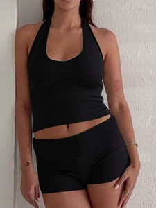 Close-up of black Y2K halter neck vest and shorts set on model against white textured wall