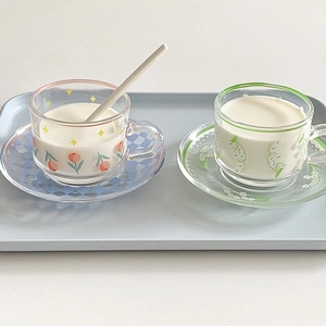 Floral glass cup and saucer set with tulip and lily designs on a light blue tray
