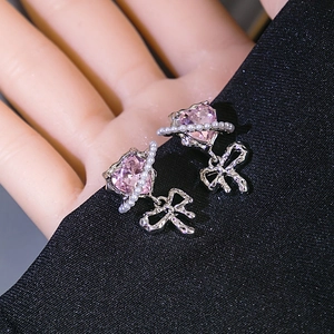 Detail of pink crystal heart earrings with silver bow and pearl studs on black fabric