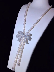 Detailed view of long pearl necklace featuring a sparkling rhinestone bow pendant on neck