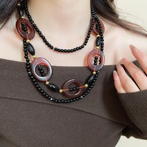 Detail of layered black beaded necklace with amber resin rings and gold accents on model