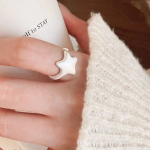 Close-up of matte white star-shaped open ring worn on finger with cozy knitted sweater