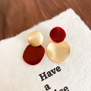 Macro detail of brushed gold asymmetric round earrings with matte red vintage coating