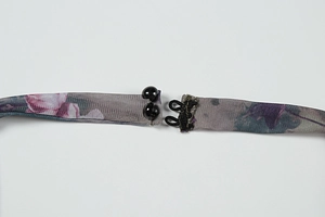 Detail of floral mesh dress straps featuring a dual black button and loop closure