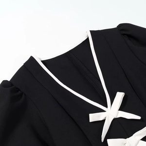 Détail du col en V sur robe noire avec bordure blanche contrastée et petit nœud