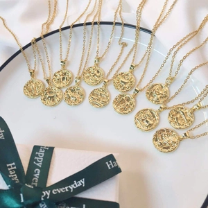 Detail of 18K gold-plated zodiac sign embossed round pendant necklaces on silk fabric
