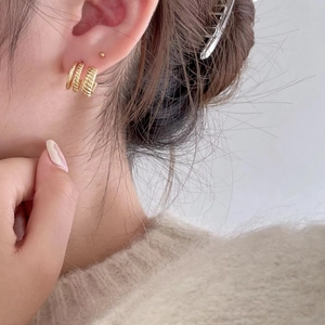 Detail of gold geometric triple-layer hoop earrings with textured twist design on model