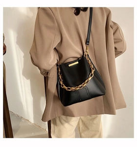 Detail of black leather bucket bag featuring a decorative gold chain and matte finish