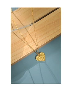 Detail shot of heart-shaped gold pendant necklace with angel relief on wooden stand
