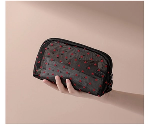 Close-up of small black mesh cosmetic bag with red hearts held in hand for size display
