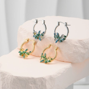 Macro shot of gold and silver hoop earrings with enamel dragonflies and daisy charms