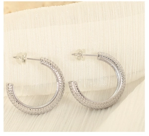 Close-up of silver C-shaped hoop earrings with intricate diamond texture on white fabric