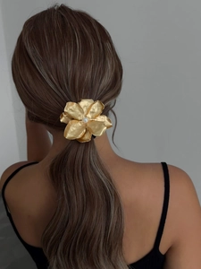 Close-up of golden flower hair tie with pearl center worn on a brunette ponytail