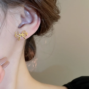 Close-up of golden bow-shaped stud earring worn on model's ear showing metal texture