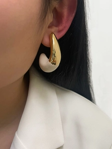 Close-up of minimalist gold teardrop earrings with cream resin inlay on woman's ear