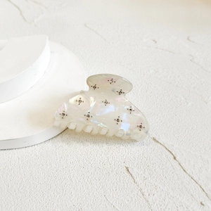 Detail of white iridescent hair claw clip with metallic stud accents on textured surface