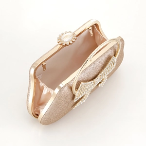 Close-up of golden evening clutch featuring diamond-encrusted bow and satin lining interior
