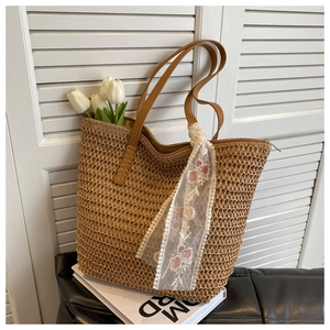 Detail of woven straw tote bag with brown leather handles and decorative floral scarf on books