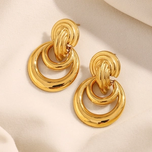 Détail de boucles d'oreilles double boucle dorées 18K sur un tissu beige