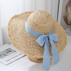 Detail of raffia sun hat with blue checkered ribbon bow and frayed edges on brim