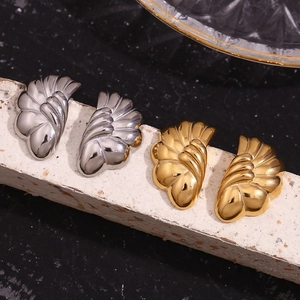 Macro detail of gold and silver wave shell wing earrings on a dark marble surface