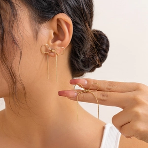 Detail of golden bow stud earring with long delicate chain tassels on model's ear