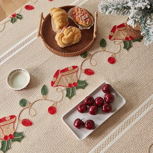 Detailed embroidery of gold bells and red holly berries on beige Christmas table runner