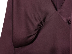 Nahaufnahme des eleganten V-Ausschnitts mit Falten auf lila Satin-Stoff der Tunika