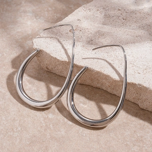 Detailed view of silver teardrop earrings placed on a textured beige stone base