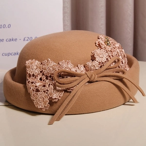 Detail of camel wool beret showing intricate lace flower appliques and a delicate bow tie