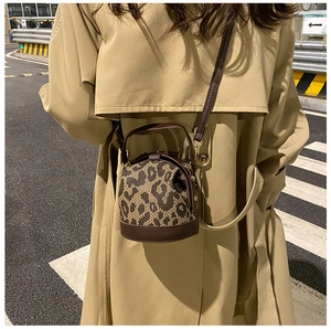 Street style shot of a leopard print cylinder bag with brown leather trim and gold hardware