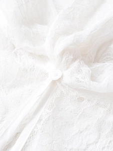 Detailed close-up of white lace fabric texture with elegant round button and ribbon tie