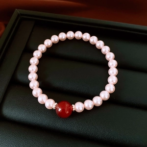 Détail du bracelet en perles roses avec une perle d'agate rouge et des entretoises