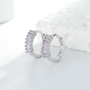 Gros plan de créoles en argent avec zircons violets taille baguette sur pierre blanche