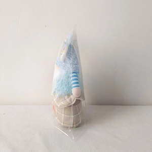 Detail of Easter gnome toy in blue knit hat and plaid fabric inside plastic packaging