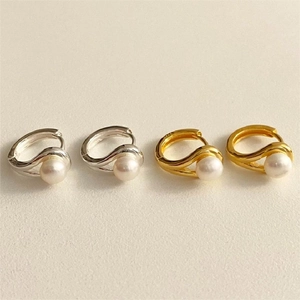 Close-up of gold and silver crossover pearl hoop earrings on beige textured background