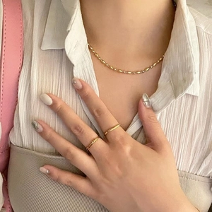Close-up of gold beaded necklace and textured rings worn with a white blouse