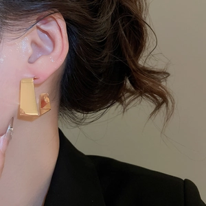 Close-up of a wide gold C-shaped geometric earring worn by a model in a black blazer