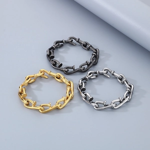 Macro detail of intertwined nail-shaped chain bracelets in gold, silver, and black finish