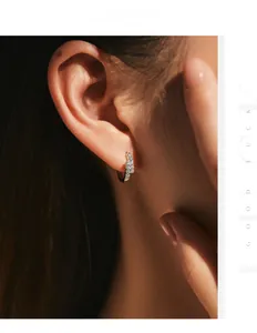 Macro shot of silver pave-set moissanite huggie earrings worn by a model
