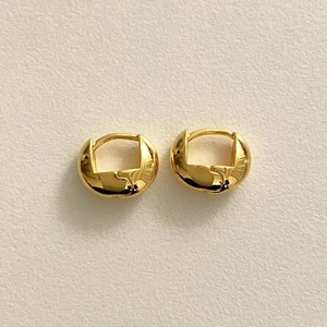 Detail of wide gold-plated 925 sterling silver hoop earrings on a textured paper background
