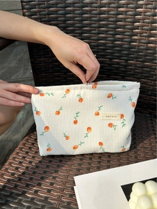 Corduroy makeup bag with orange fruit pattern and top zipper on a wicker chair