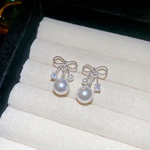 Elegant silver bow earrings with zircon and pearls on beige velvet jewelry display