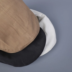 Close-up of three cotton twill flat caps in khaki, black, and white with neat stitching