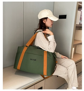 Detail of a dark green canvas travel bag featuring orange straps and a large front pocket
