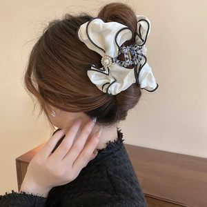 Detail of large cream fabric bow claw clip with black piping and pearl center on hair