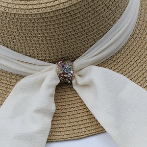 Detailed macro view of straw sun hat featuring a white fabric ribbon and colorful rhinestones