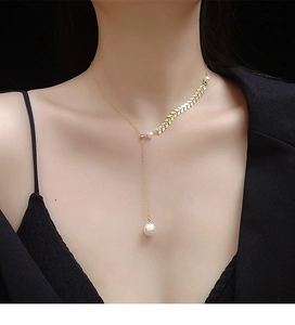 Detail of a golden wheat leaf Y-necklace featuring two elegant pearls on a black background